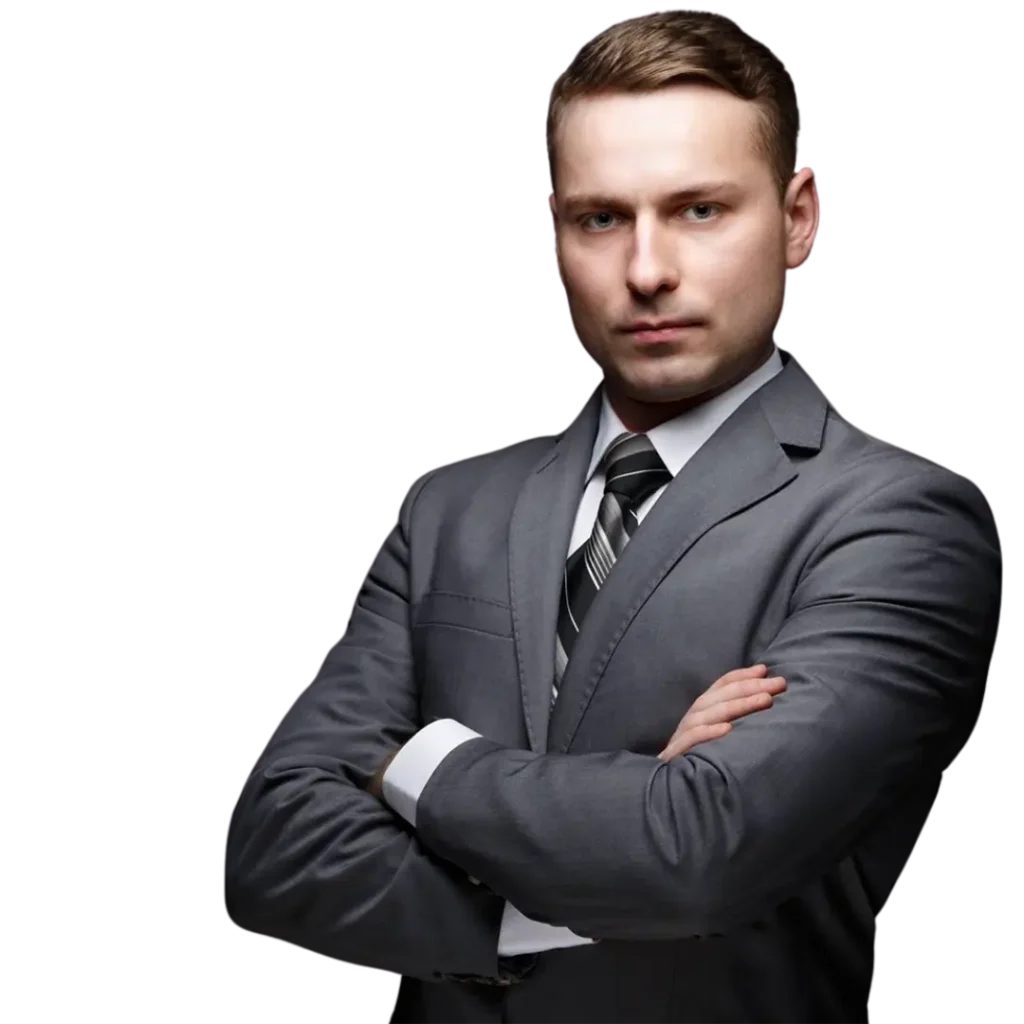 Kanclerz Uczelni Łukaszewski Adrian Łuczak Na zdjęciu znajduje się młody mężczyzna o krótkich, starannie ułożonych jasnobrązowych włosach i ostrych, wyrazistych rysach twarzy. Ma jasną cerę, niebieskie oczy oraz stanowcze, skoncentrowane spojrzenie. Jego usta są zamknięte, a wyraz twarzy poważny, co nadaje mu profesjonalny i zdecydowany wygląd. Jest ubrany w elegancki, dobrze skrojony szary garnitur, pod którym widać białą koszulę oraz czarno-srebrny krawat w skośne pasy. Marynarka jest idealnie dopasowana do sylwetki, a mankiety koszuli delikatnie wystają spod rękawów, dodając stylizacji formalnego charakteru. Jego postawa jest pewna siebie – stoi z założonymi rękami, co może sugerować stanowczość i profesjonalizm. Czarne, jednolite tło podkreśla jego sylwetkę, sprawiając, że postać dominuje w kadrze, a całość wygląda jak zdjęcie biznesowe lub korporacyjne portretowe ujęcie.