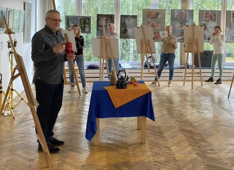 Na zdjęciu przedstawiono wnętrze, w którym na podłodze stoi sztaluga z obrazem, a w tle widoczne są meble i elementy wyposażenia wnętrza , sugerujące prowadzenie zajęć praktycznych (zajęcia praktyczne) z malarstwa i historii sztuki (malarstwo i historia sztuki) na studiach podyplomowych (studia podyplomowe).